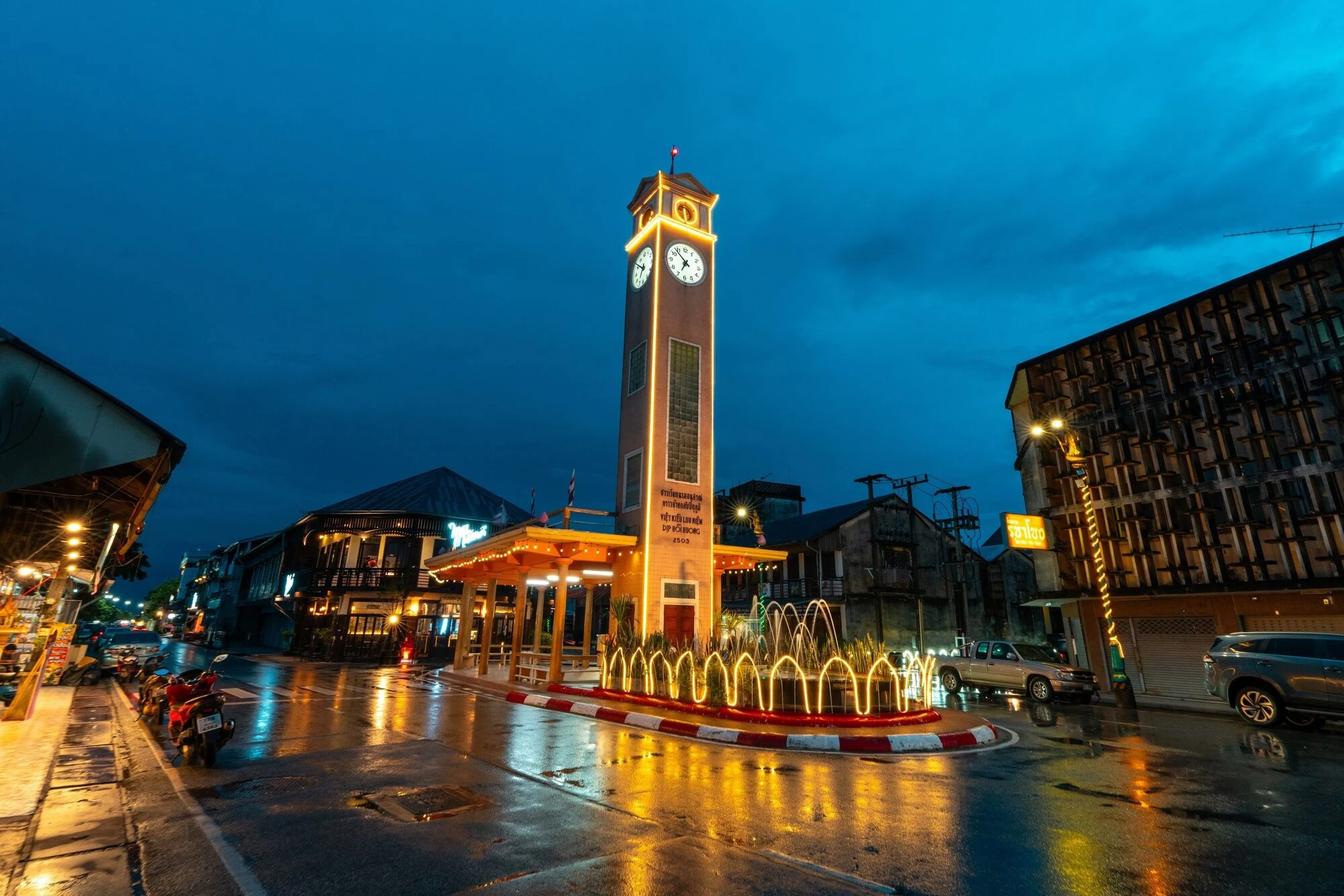 A clocktower that is lit up at night with a fountain at its base.