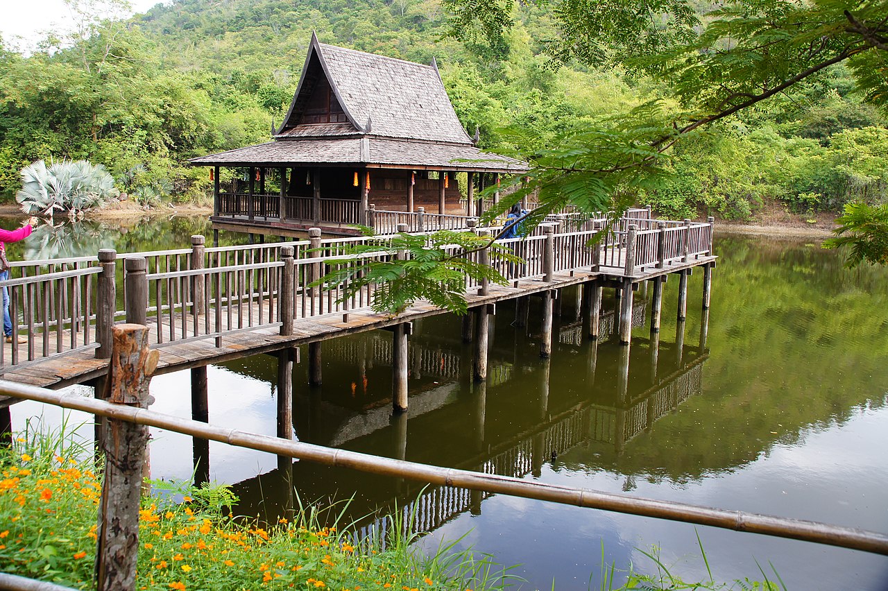 A stilted Thai wooden house on the water over a lake and surrounded by lush jungle.